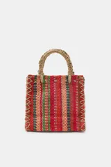 Mini bolso cuadrado de yute 100%, con diseño de rayas multicolor en tonos rojos, verdes y tostados. Cuenta con asas de mano rígidas forradas en yute y costuras decorativas entrelazadas en los laterales.