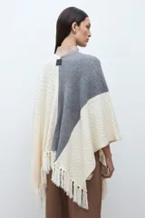 Ruana de tejido de punto con diseño color block en tonos crudo, gris y negro, con terminación de flecos en el ruedo y textura en relieve.