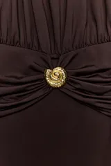 Vestido midi de cuello halter con detalle de drapeado en la cintura y broche metálico dorado en forma de caracola. Presenta cierre ajustable con lazadas en la espalda.