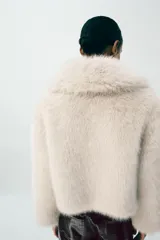 Abrigo corto de piel sintética en color negro, con cuello de solapa amplio, manga larga y cierre frontal con corchetes ocultos.