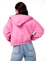 Chaqueta corta de lona color rosa, con capucha ajustable, cierre frontal y forro interior acolchado negro. Presenta un parche con el logo de la marca en el pecho.