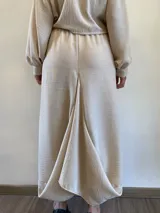 Pollera midi de corte asimétrico y holgado, inspirada en la forma de pantalón babucha. Confeccionada en tela crepé color beige, presenta cintura elástica, bolsillos laterales amplios y un detalle de etiqueta con texto en el bolsillo derecho.