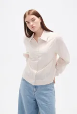 Camisa de algodón con estampado de rayas verticales finas en tonos beige y blanco, cuello clásico, cierre frontal con botones y mangas largas con puños anchos estructurados.