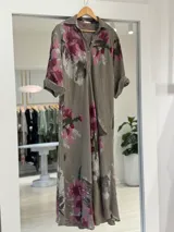 Vestido largo color visón con estampado floral en tonos fucsia y verde, de corte recto, con mangas largas arremangables, cuello camisero y cierre frontal parcial con botones.