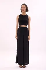 Pantalón largo de tiro alto, color rosa pálido, de corte ancho y fluido. Presenta una hilera de recortes ovalados decorativos a lo largo de la costura lateral.