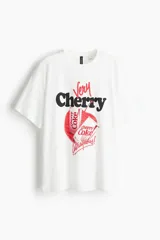 Remera blanca de algodón con estampado gráfico de Coca-Cola Cherry, que incluye las palabras "Very Cherry" y "Outrageous!".