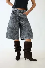 Bermuda de denim gris con acabado jaspeado y textura desgastada. Presenta un corte amplio y recto que cae por debajo de la rodilla, con bolsillos delanteros y traseros funcionales, trabillas para cinturón y cierre frontal con botón y cremallera.