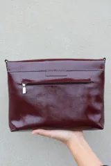 Sobre de mano color bordó en cuero charolado, con solapa frontal decorada con una piedra ágata natural engarzada. Incluye correa larga extraíble y cierre trasero.