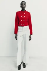 Cazadora de estilo militar en color rojo, con cuello redondo, manga larga y cierre frontal mediante alamares con botones dorados. Presenta trabillas con botón en los hombros y detalle de costuras en los puños.