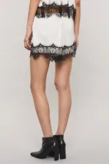 Short de satén texturado color blanco, de tiro medio con elástico en la cintura y detalle de puntilla estilo chantilly negra en el ruedo.