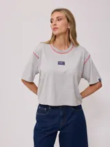 Remera blanca de algodón con corte cropped y calce holgado. Tiene cuello redondo con ribete azul y logo de la marca estampado en el pecho.