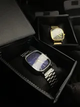Reloj Casio Quartz con caja cuadrada plateada, esfera azul intenso, manecillas y marcadores de hora dorados, y correa de acero inoxidable plateada. Incluye función de fecha.