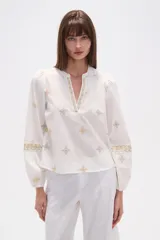 Blusa de algodón color blanco con cuello mao y escote en V. Presenta mangas largas abullonadas con puños elásticos y detalles de bordados geométricos en tonos ocres y verdes distribuidos por toda la prenda.