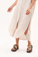 Vestido camisero largo de lino color beige, con silueta relajada, abotonado al frente, cuello camisero, mangas regulables y tajos laterales.