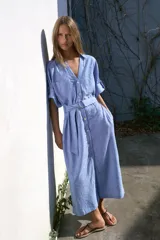 Vestido midi de cuello solapa con escote en pico y mangas tres cuartos ajustables con trabilla. Cuenta con bolsillos delanteros de plastrón, bolsillos laterales ocultos en costura, cierre frontal con botones y cinturón ajustable del mismo tejido con hebilla metálica circular.