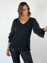 Blusa negra con escote en V y mangas largas abullonadas de tela semitransparente con textura. El cuerpo de la blusa es de tejido liso.