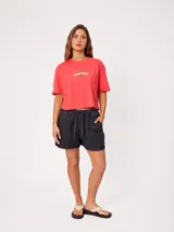 Remera coral cropped, de manga corta, con estampa trasera colorida de un perro surfeando y el texto "Rusty County Surf Club".