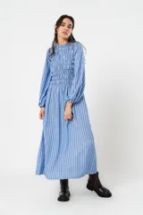 Vestido largo a rayas verticales azules y blancas, con manga globo y diseño de nido de abeja con hilo elástico hasta la cintura. Cuello alto fruncido y falda amplia con caída fluida.