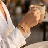 Pulsera elástica de cuentas doradas con baño de oro, intercaladas con dijes de ojos turcos en tonos azul, blanco y negro.