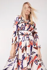 Vestido largo de viscosa con estampado abstracto en tonos blanco, naranja quemado, marrón y azul oscuro. Presenta cuello redondo ribeteado en negro, mangas largas abullonadas y talle marcado con un cinturón ancho ribeteado en negro.