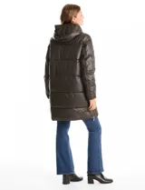 Campera puffer larga de color marrón oscuro, con diseño capitoneado de costuras horizontales. Presenta un sistema de cierre doble con pechera interna fija con cierre y cuello alto, y cierre frontal exterior con botones a presión. Incluye bolsillos frontales amplios, capucha fija y cierres laterales en el ruedo para mayor movilidad.