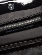Maxibolso Judy de Mishka, confeccionado en símil charol negro con efecto arrugado. Cuenta con apertura de broche imán, asas para llevar al hombro con detalle de nudo y un diseño grande y liviano.