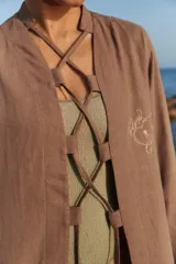 Túnica larga de lino y rayón color marrón, con diseño abierto, mangas largas y lazos ajustables en el frente. Presenta un bordado sutil a tono en el pecho.