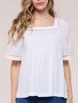 Blusa de corte holgado color marfil, confeccionada en mezcla de modal y algodón, con escote cuadrado y mangas cortas adornadas con detalles de puntilla calada.