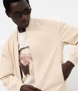Campera tipo bomber masculina de color beige, con cuello, puños y ruedo acanalados. Presenta cierre frontal por cremallera, bolsillos laterales y acabado con tecnología repelente al agua.