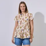 Blusa color crema con estampado tribal en tonos marrón, verde y azul. Tiene cuello a la base, escote en V, abertura central con botones, corte en la cintura con volados y ruedo con volados.