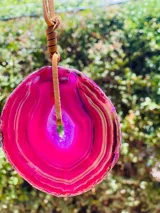 Collar con dije de piedra ágata blanca y marrón, con forma circular irregular y agujero en el centro. El dije está sujeto con un cordón fino de cuero marrón.