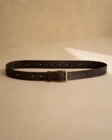Cinto de cuero marrón oscuro, con hebilla metálica dorada envejecida y detalles de tachas y apliques de cuero entrelazado.