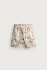 Bermuda cargo color negro de corte relaxed fit, confeccionada en tejido de algodón con elasticidad y efecto lavado. Cuenta con cintura elástica ajustable con cordón, bolsillos frontales y bolsillos laterales tipo cargo con solapa en las perneras.