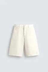 Bermuda de denim color crudo o blanco roto, de corte ancho (baggy fit) y largo hasta la rodilla. Presenta cinco bolsillos, bordado a tono en el frente y un parche con logo en la parte trasera.