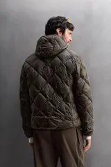 Campera puffer verde oliva acolchada con diseño de rombos, capucha y cierre frontal con cremallera. Incluye bolsillos laterales con cierre. Relleno de plumón y plumas.