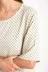 Blusa cruda con estampado de lunares negros, de manga corta y cuello redondo.