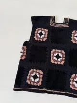 Chaleco sin mangas, confeccionado con cuadrados de cuero negro perforado combinados con cuadrados de crochet en hilo de algodón negro y blanco, con detalles centrales en rojo.