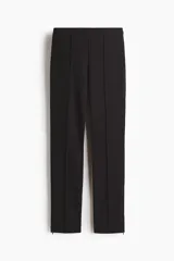 Pantalón de punto elástico en color negro, de corte ajustado con pliegue cosido frontal y cierre en los bajos.