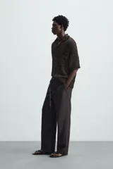 Polo de punto de calce relajado, color marrón oscuro jaspeado con negro. Presenta cuello solapa con abertura frontal en V y mangas cortas.