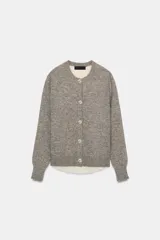 Chaqueta de punto de cuello redondo y manga larga, con diseño combinado que incluye una capa interior en tono crudo. Presenta cierre frontal con botones y puños acanalados.