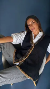 Chaleco tejido color tostado con destellos de lurex, escote en V y cierre frontal con botones. Presenta detalles de bordados y terminaciones en crochet en color crudo.