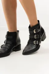 Botas cortas de cuero negro con puntera fina, taco bajo y cierre lateral. Presentan tres correas con hebillas plateadas y apliques de tachas plateadas.