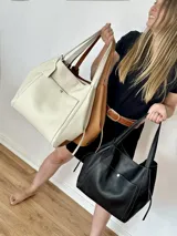 Bolso tipo tote extra grande confeccionado en cuero genuino color natural, de diseño amplio y sin forro interior. Cuenta con bolsillo frontal externo con solapa y botón a presión metálico, parche de cuero grabado en la base y doble asa de hombro.