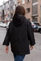 Parka liviana color beige con capucha, cierre frontal con botones, bolsillos delanteros con tapa y ajuste en la cintura. Presenta mangas con puños vueltos y detalle de botones.