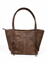 Cartera tipo tote bag de cuero vacuno marrón, con detalles de trenzado artesanal en los laterales y flecos colgantes decorativos. Cuenta con doble asa de hombro y cierre superior.
