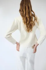 Chaqueta de punto color negro, con escote en pico, manga larga y cierre frontal con botones dorados. Presenta un diseño con bajo asimétrico.