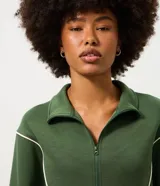 Campera deportiva de microfibra color verde oscuro, con cuello alto, manga larga y cierre frontal. Presenta recortes estructurados con vivos contrastantes claros, barra ajustada y puños alargados.
