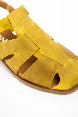 Sandalia tipo cangrejera de cuero lavado color mostaza, con diseño de tiras cruzadas, puntera cerrada y cierre con hebilla metálica en el tobillo. Cuenta con suela plana de goma.