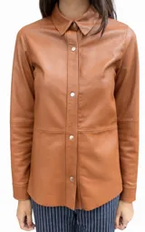 Camisa de cuero ovino color suela, con cuello camisero, cierre frontal mediante broches metálicos a presión, manga larga con puño y corte recto.