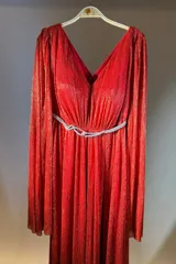 Vestido largo plisado color rojo con hilos dorados brillantes, escote en V pronunciado y mangas largas. Incluye un cinturón fino plateado con nudo decorativo.